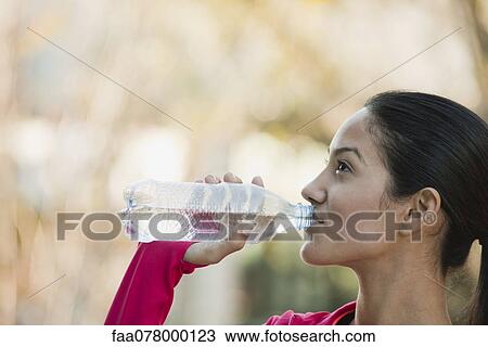Stock Image - Young woman drinking bottle of water. Fotosearch