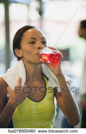 Stock Image - Young woman drinking sports drink after exercising. Fotosearch