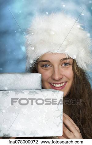Stock Image - Young woman holding Christmas presents, portrait. Fotosearch