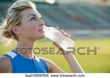 Picture - Young woman hydrating, taking break from exercising. Fotosearch