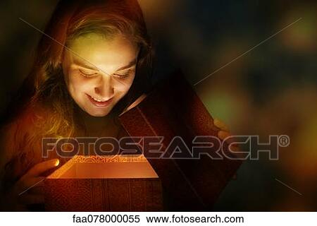 Stock Photography - Young woman illuminated by golden light as she opens Christmas present. Fotosearch