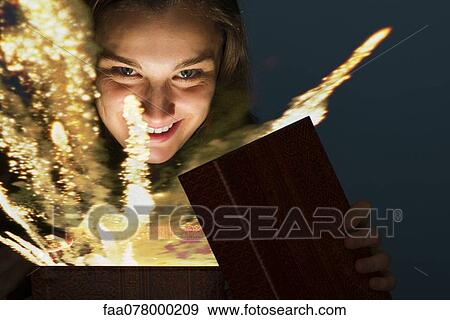 Stock Photo - Young woman opening gift box containing glowing fireworks. Fotosearch