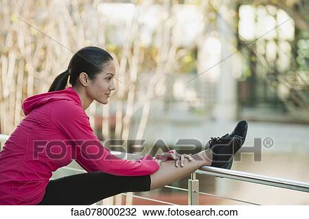 Stock Image - Young woman stretching leg on railing. Fotosearch