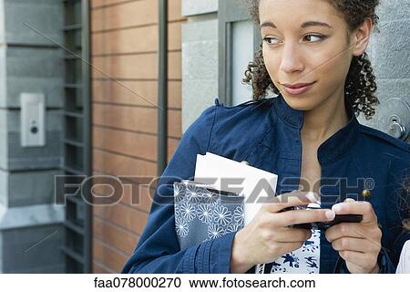 Stock Image - Young woman text messaging outdoors. Fotosearch