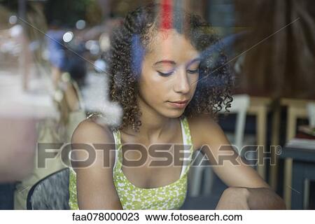 Stock Image - Young woman viewed through window, looking down in thought. Fotosearch