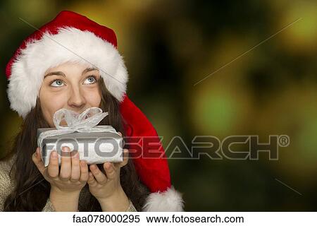 Young woman wearing Santa hat, holding Christmas present in front of mouth View Large Photo Image Stock Photography - Young woman wearing Santa hat, holding Christmas present in front of mouth. Fotosearch