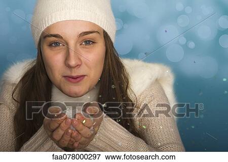 Stock Photo - Young woman wearing winter clothing, holding handful of confetti, portrait. Fotosearch