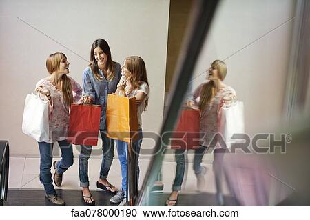 Young women carrying shopping bags, standing at bottom of escalator View Large Photo Image Stock Image - Young women carrying shopping bags, standing at bottom of escalator. Fotosearch
