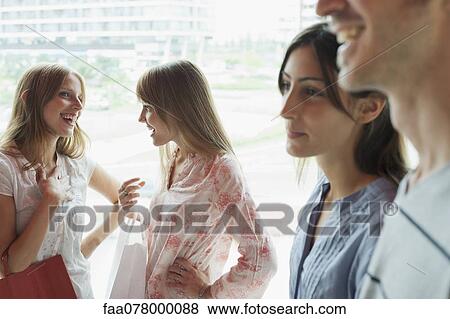 Stock Photo - Young women chatting, people passing by in foreground. Fotosearch
