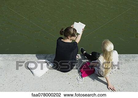 Stock Image - Young women relaxing together beside canal. Fotosearch