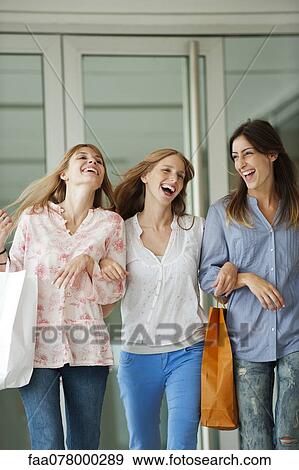 Stock Photo - Young women walking together, carrying shopping bags. Fotosearch