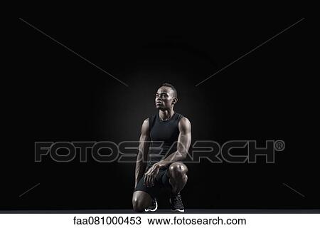 Stock Image - Athlete crouching, looking away in thought. Fotosearch