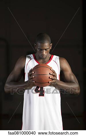Stock Image - Basketball player holding basketball, portrait. Fotosearch