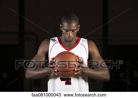 Stock Image - Basketball player holding basketball, portrait. Fotosearch
