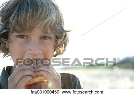 Stock Image - Boy eating sandwich outdoors, portrait. Fotosearch