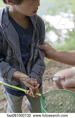 Stock Image - Boy holding fishing net, mid section. Fotosearch