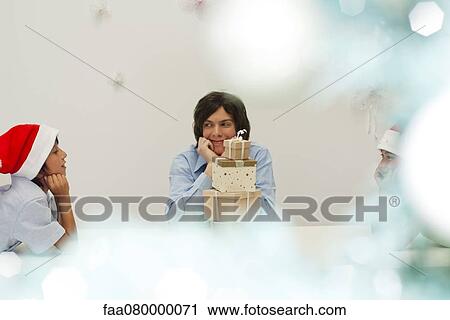 Stock Image - Brothers sitting around stack of Christmas presents, looking at each other in anticipation. Fotosearch