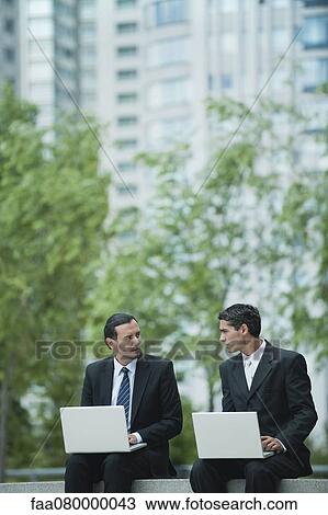 Stock Image - Business associates sitting outdoors with laptop computers. Fotosearch