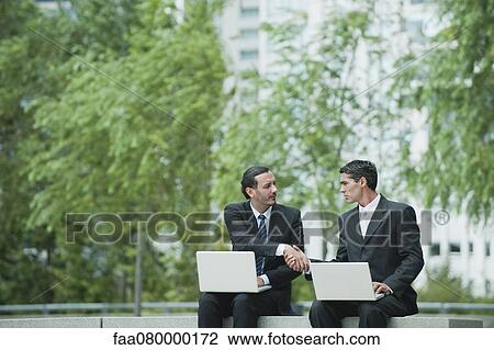 Business executives sitting outdoors with laptop computers, shaking hands View Large Photo Image Stock Image - Business executives sitting outdoors with laptop computers, shaking hands. Fotosearch