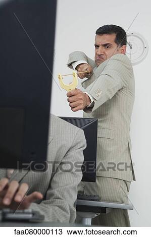 Stock Image - Businessman aiming slingshot at colleague. Fotosearch