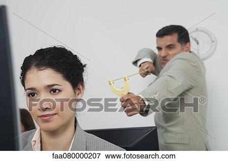 Stock Photo - Businessman aiming slingshot at young female colleague. Fotosearch