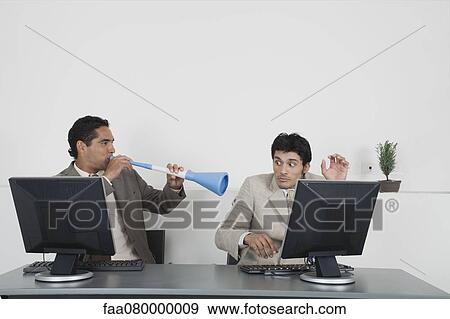 Stock Photo - Businessman blowing vuvuzela horn into colleague's ear. Fotosearch