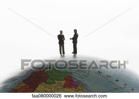 Stock Photograph - Businessman figurines standing on top of globe, silhouette. Fotosearch