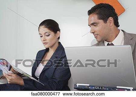 Stock Photo - Businessman with laptop computer looking over while businesswoman reads magazine. Fotosearch