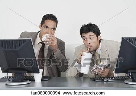 Picture - Businessmen eating fast food at desk in office. Fotosearch