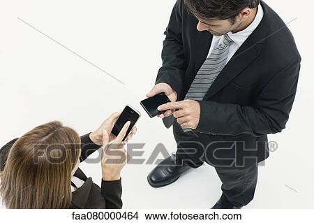 Picture - Businesswoman and businessman standing face to face, both using smartphones. Fotosearch