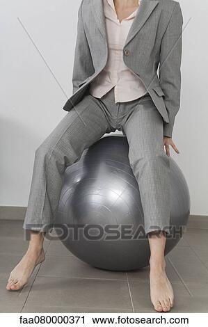 Stock Image - Businesswoman boucing on fitness ball, cropped. Fotosearch