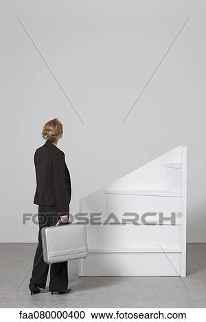 Stock Image - Businesswoman standing before incomplete staircase, rear view. Fotosearch