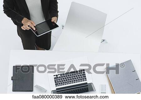Stock Photo - Businesswoman standing by desk using digital tablet, high angle view. Fotosearch