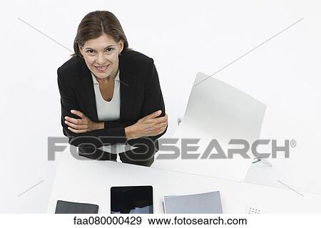 Stock Photo - Businesswoman standing by desk with arms folded. Fotosearch