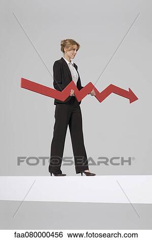 Businesswoman walking on balance beam, carrying large arrow indicating profits View Large Photo Image Stock Photograph - Businesswoman walking on balance beam, carrying large arrow indicating profits. Fotosearch