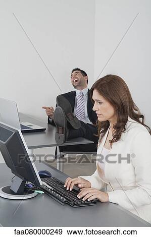 Stock Photo - Businesswoman working in office while colleague laughs in background. Fotosearch