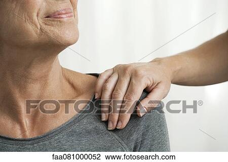 Stock Image - Comforting hand on senior woman's shoulder, cropped. Fotosearch