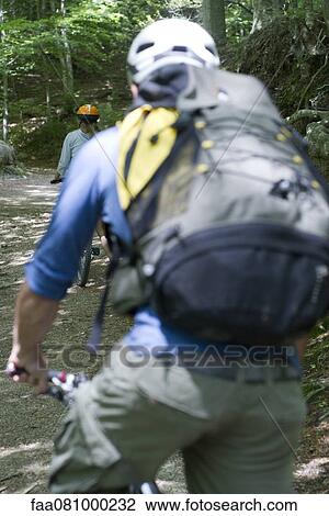 Stock Image - Cyclists biking through woods. Fotosearch