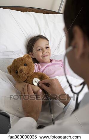 Stock Photography - Doctor comforting young patient by examining her teddy bear with a stethoscope. Fotosearch