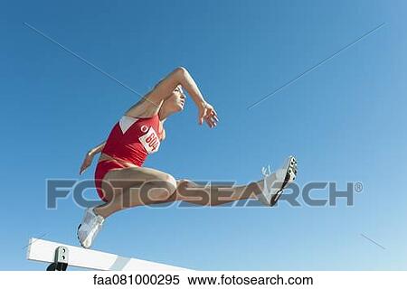 Stock Photography - Famale athlete jumping over hurdle, low angle view. Fotosearch