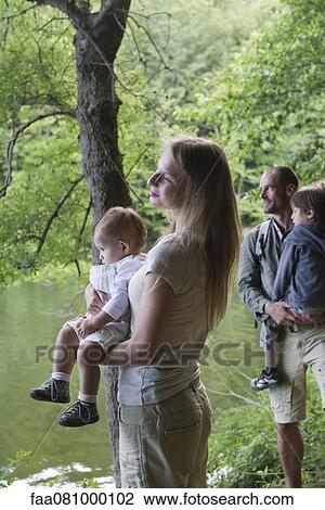 Stock Image - Family in woods looking at river, focus on mother holding baby girl. Fotosearch