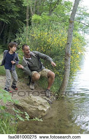 Stock Photography - Father and son throwing pebbles into river. Fotosearch