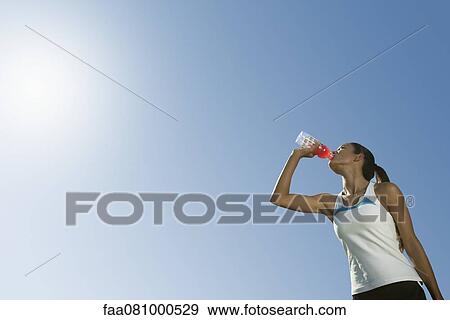 Female athlete drinking sports drink, low angle view View Large Photo Image Stock Photo - Female athlete drinking sports drink, low angle view. Fotosearch