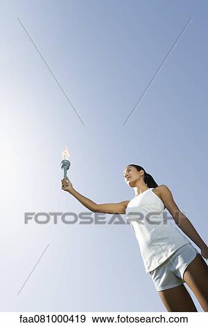 Stock Photo - Female athlete holding up torch, low angle view. Fotosearch
