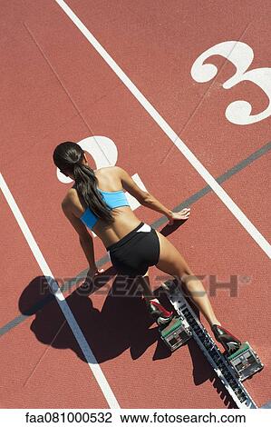 Stock Image - Female athlete in starting position on running track, rear view. Fotosearch
