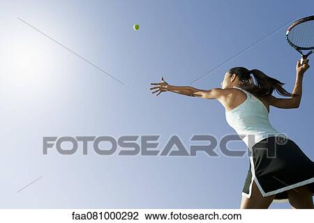 Stock Image - Female tennis player serving ball, low angle view. Fotosearch