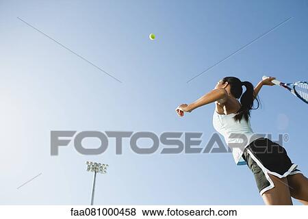 Stock Photo - Female tennis player serving ball, low angle view. Fotosearch