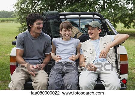 Stock Image - Friends sitting in back of pick-up truck, laughing. Fotosearch