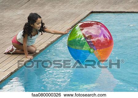 Stock Photograph - Girl crouching beside pool, playing with beach ball. Fotosearch