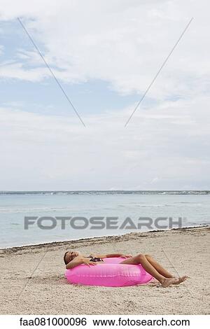Stock Photograph - Girl lying on infltable ring on beach with eyes closed. Fotosearch